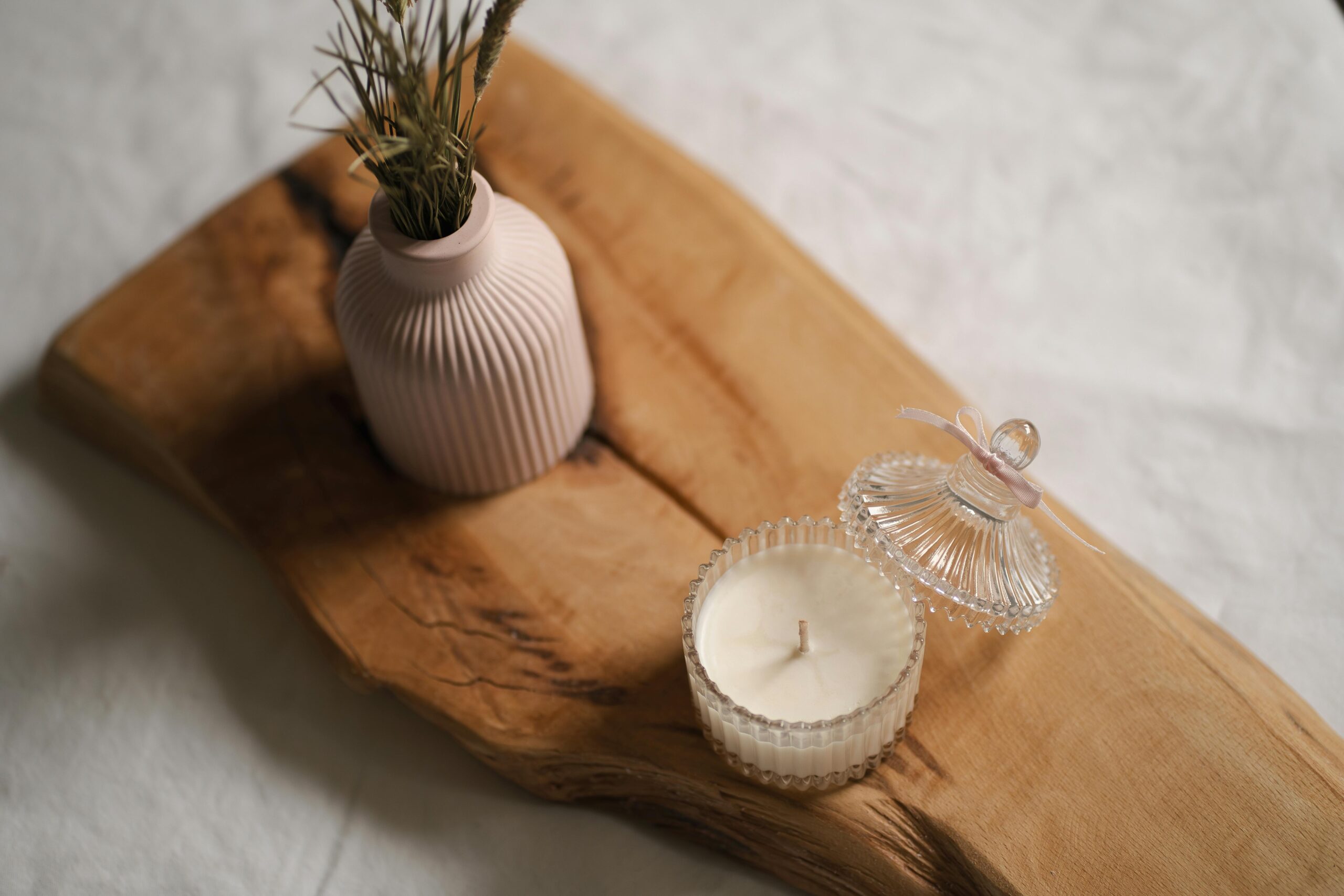 Elegant minimalist arrangement with a scented candle and decorative vase on a wooden board.